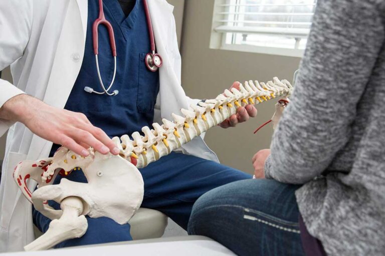Person in comfortable clothing discussing back pain with a chiropractor in a bright examination room.