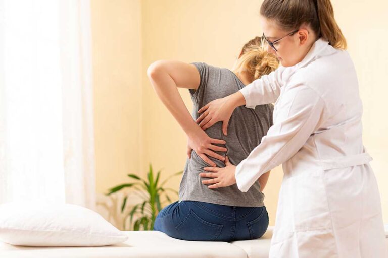 Woman resting with a heating pad and symptom journal beside her while discussing lower-back discomfort.
